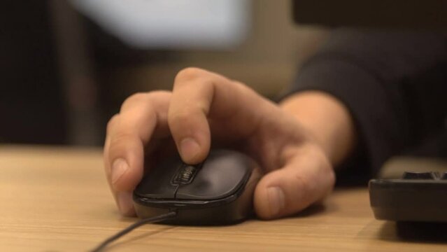 Office worker scrolls black computer mouse wheel with index finger on wooden table on blurred background extreme closeup