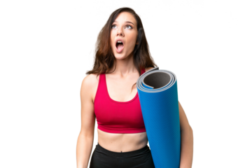 Young sport woman going to yoga classes while holding a mat over isolated background looking up and with surprised expression