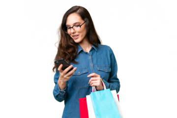 Young caucasian woman over isolated background holding shopping bags and writing a message with her cell phone to a friend