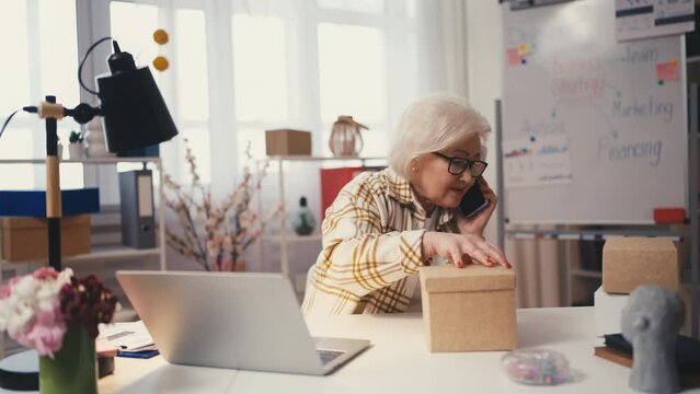 Busy senior woman talking on phone and packing orders for clients, business