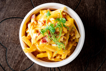 Salted French fries with bacon and cheese sause in white bowl on a wooden table