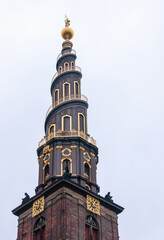 Copenhagen, Denmark - September 14, 2010: Vor Frelsers church. Tower closeup against light blue sky. Golden trim of spiral and clock. Statues on corniche and on golden globe at top