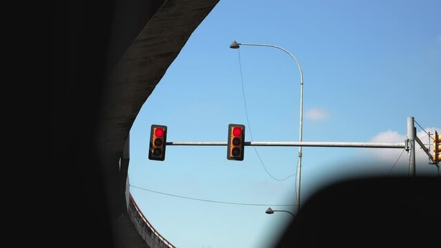 View from a car on a two hanging traffic lights on a pillar under the bridge at a crossroad. Red light and blue sky on the background 