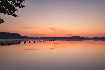 Fototapeta premium See im Abendrot - Sunset - Landscape - Beautiful Sunset scene over the lake and silhouette hills in the background - Sunrise over sea - Colorful - Reed - Clouds - Sky - Sundown - Sun 