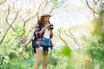 Asian female tourist backpacking in hat taking pictures with camera and going for a tropical forest walk summer nature tourism happy long holiday activities holiday travel concept
