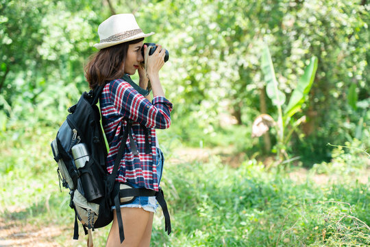 Asian female tourist backpacking in hat taking pictures with camera and going for a tropical forest walk summer nature tourism happy long holiday activities holiday travel concept