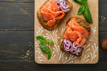 Sandwiches or toasts with salted salmon, avocado guacamole, red onions and basil on old dark wooden background. Set of danish open sandwiches. Healthy food, breakfast. Dieting food concept. Top view.