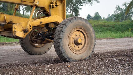 close up of motor grader tires leveling stones and gravel for road repairs in Lampung
