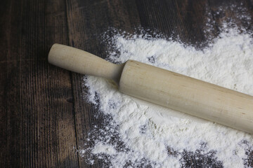 Wooden light rolling pin for dough lies in flour on a dark wooden table. Flour for dough on countertop in kitchen