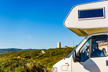 Caravan on spanish coast, lighthouse in distance - obrazy, fototapety, plakaty