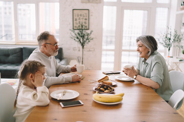 Grandparents talking while having breakfast with grandchild