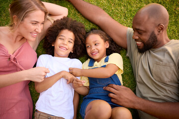 Overhead Shot Of Multi-Racial Family Lying On Grass Tickling Children