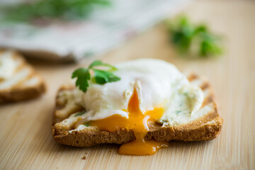 Fried toast bread with spread and poached egg, on a wooden table.