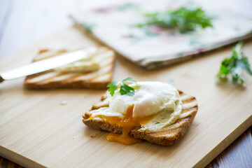 Fried toast bread with spread and poached egg, on a wooden table.