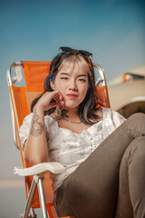 Asian girl seating in a beach chair with a volkswagen beetle in a blue sky behind.