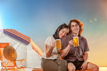 Interracial couple toasting draft beer against the sunset.