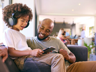 Obraz premium Father And Son Using Digital Tablet With Headphones At Home With Multi-Generation Family Behind