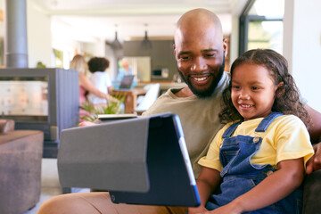 Father And Daughter Using Digital Tablet At Home With Multi-Generation Family In Background