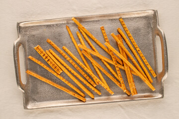 Straw is a bakery product. A few straws with a metal tray on a white linen cloth, macro, top view.