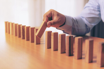 Wooden game strategy, Businessman hand stopping falling wooden dominoes effect from continuous toppled or risk, strategy and successful intervention concept for business.