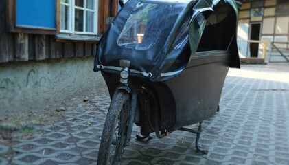 Black dirty E-cargo bike parking in Berlin. Bright summer day. Eco friendly nature trip.