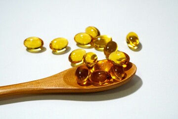 Rice bran oil capsule on wooden spoon and white background.