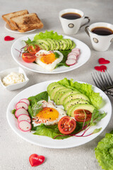 Fototapeta na wymiar Romantic couple breakfast - two portions heart-shaped fried eggs with avocado, spinach, cherry tomato and radish on plates and two cups of coffee