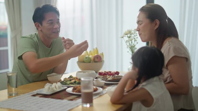 asian happy family spend time have breakfast or dinner on table together at sunlight.Little kid daughter enjoy eat yummy food with father,asian mother.asia family day meet talk at home
