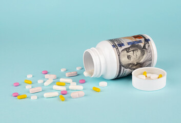 Pills spilling out of pill bottle on blue background with copy space. The concept of expensive...