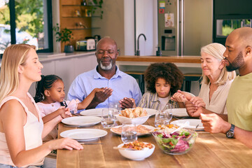 Multi-Generation Family Holding Hands And Saying Prayer Before Meal At Home 