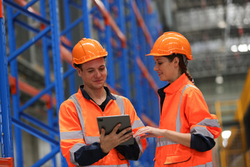 Industrial engineer discussing work in factory , logistic engineers team wearing orange safety helmets and vests standing in a warehouse with high-rack background. 