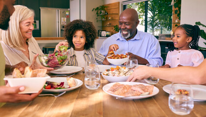 Multi-Generation Family Sitting Around Table Serving Food For Meal At Home 