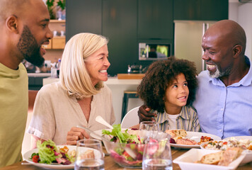 Multi-Generation Family Sitting Around Table Serving Food For Meal At Home 