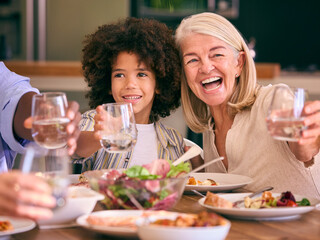 Multi-Generation Family Doing Cheers With Water As  They Sit Around Table Having Meal At Home 