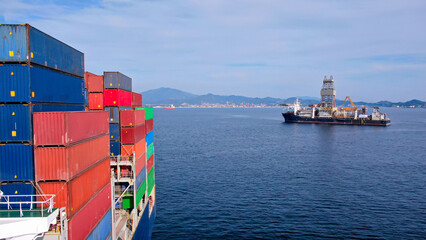 View on large offshore drill ship from ultra large container ship with loaded containers on board.