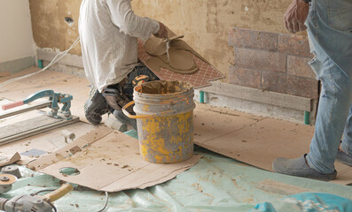 A foreman applying cement to a tile while his assistant stands beside him. Construction and...