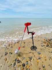 metal detecting equipment detector and sand scoop on the beach with ocean sand waves and sky behind...