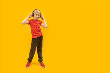 Fototapeta na wymiar Full-length portrait of teenage boy in sportswear with headphones on his head in isolation on yellow background. Copy space.