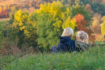 Two siblings sit hugging on grass on autumn landscape background. Carefree childhood. Back view