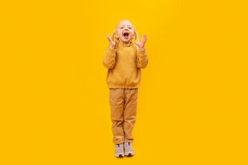 Little girl is surprised or screams. Full-length portrait of preschool girl in yellow suit on yellow background.