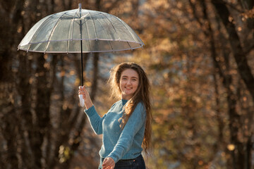 Cheerful blue-eyed girl with wavy hair dance with transparent umbrella in hands in autumn forest or park