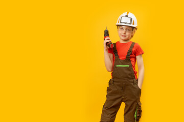 Portrait of boy in work overalls and helmet with drill in his hands. Role of construction worker....