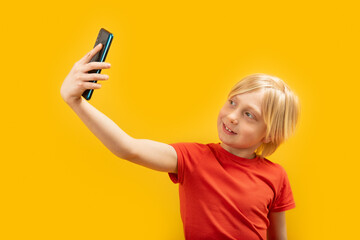 Portrait of blond boy in red T-shirt with phone in his hands. Child takes selfie. Isolated on...