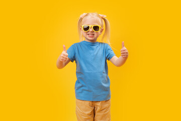 Fototapeta na wymiar Portrait of girl in blue T-shirt and sunglasses showing thumbs up or like gesture with two hands. Copy space, mock up