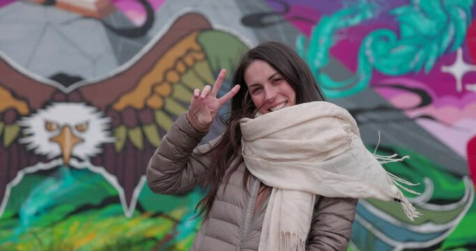 Young woman outdoors in autumn gives peace sign towards camera