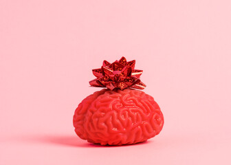 Human brain model with red festive bow on pastel pink background. Creativity, inspiration and mental health concept