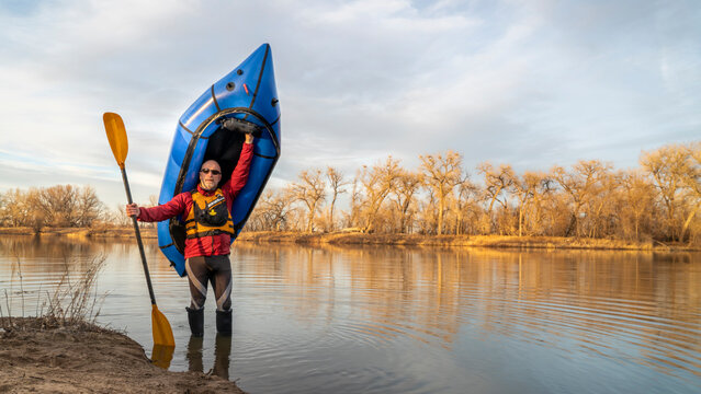 happy senior male  paddler is standing with an inflatable packraft and paddle on a lake shore in early spring spring in northern Colorado