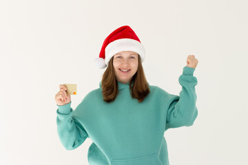 Fototapeta na wymiar Excited pregnant young caucasian woman in Christmas hat holding credit card and making success gesture isolated on white background