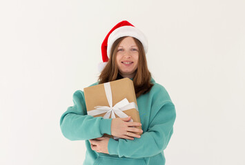 Pretty overjoyed lady holding large giftbox close to chest wear green hoodie and santa hat isolated white background