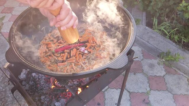 Cooking Uzbek pilaf. Cooking zirvak in a cast-iron cauldron on the grill. Adding pepper with a wooden hand mill